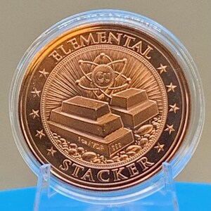 Straight-on reverse of the Night Arrival 1 oz copper round in its capsule: "Elemental Stacker" lettering around a stack of copper bars beneath an atom symbol, ringed by stars