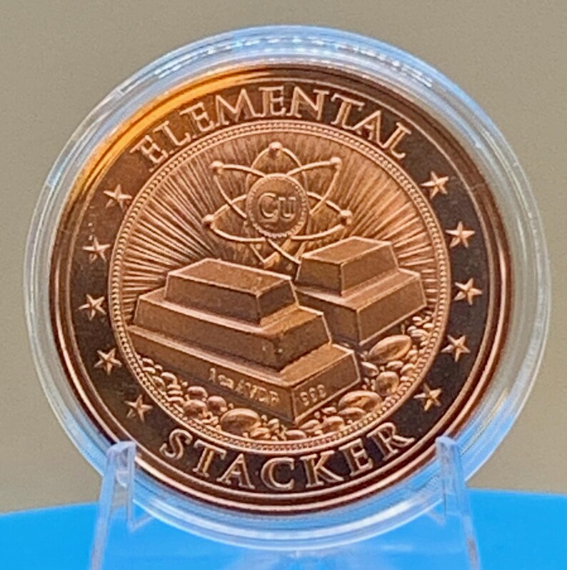 Straight-on reverse of the Night Arrival 1 oz copper round in its capsule: "Elemental Stacker" lettering around a stack of copper bars beneath an atom symbol, ringed by stars