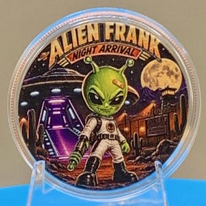 Front of the Night Arrival 1 oz copper round in a clear capsule: a colorized green alien with a bandage on his head, in a white spacesuit, stands before a landed UFO with a glowing purple ramp under a full moon, with "Alien Frank Night Arrival" lettering