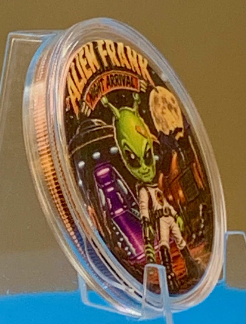 Angled view of the Night Arrival 1 oz copper round in its capsule showing the colorized green alien and purple UFO face and the rim of the coin