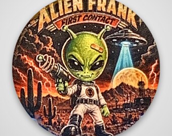 May include: A circular pinback button featuring a green alien character in a white spacesuit holding a ray gun. The background shows a desert landscape with cacti, a full moon, and a flying saucer. The text reads ALIEN FRANK FIRST CONTACT.