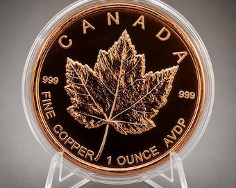 May include: A round copper coin encased in a clear plastic protective capsule. The coin features a detailed maple leaf at the centre, with the text CANADA, 999, FINE COPPER, and 1 OUNCE AVDP embossed on the metallic surface of the coin.