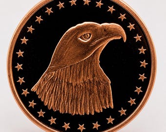 May include: A circular copper-toned coin featuring a relief of an eagle head in profile at the center. The background is black, surrounded by a border of twenty-four small copper-toned stars arranged in a circle along the outer edge of the coin.