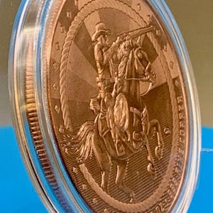 Angled side view of the 5 oz .999 fine copper Cowboy round in its capsule, showing the round's edge and rim detail.