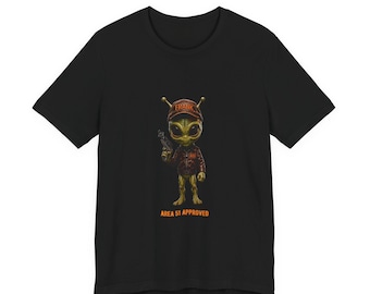 May include: A black short-sleeved t-shirt featuring a graphic of a green alien character wearing a brown cap with the text FRANK, a brown jacket, and holding a small silver device. Below the character is the text AREA 51 APPROVED.