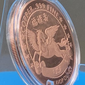 Encapsulated 2026 Year of the Horse copper round tilted on a blue stand showing the Pegasus reverse at an angle, with light catching the high-relief wings and the capsule's reeded rim.
