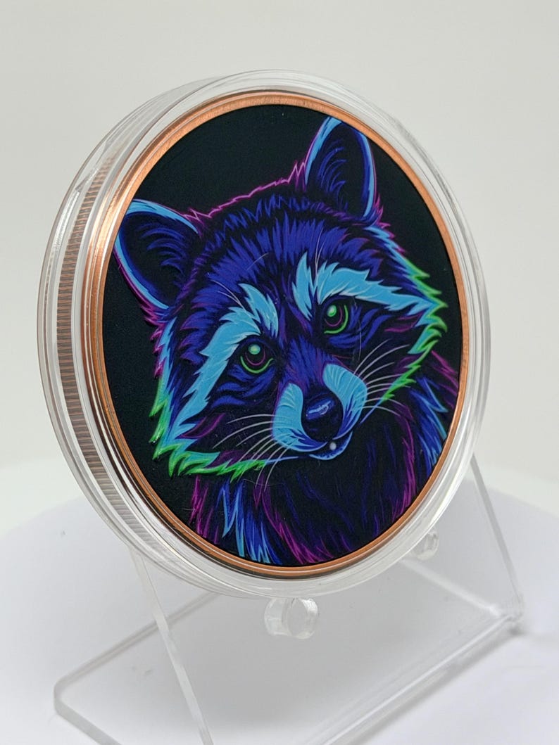 May include: A circular collectible coin featuring a vibrant, neon-colored illustration of a raccoon against a black background. The raccoon is rendered in shades of blue, purple, and green. The coin has a copper-toned rim and a clear protective casing.