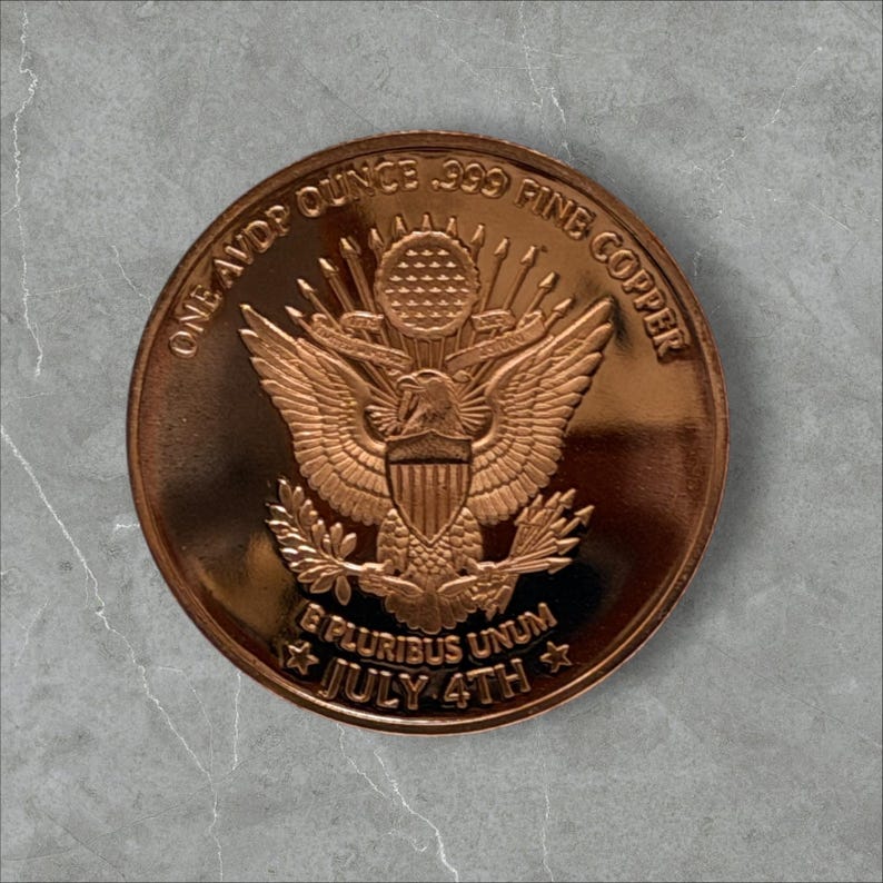 Reverse of a 1 oz .999 fine copper round showing the Great Seal eagle with shield, arrows and olive branch, inscribed One AVDP Ounce .999 Fine Copper, E Pluribus Unum and July 4th, on a gray stone background