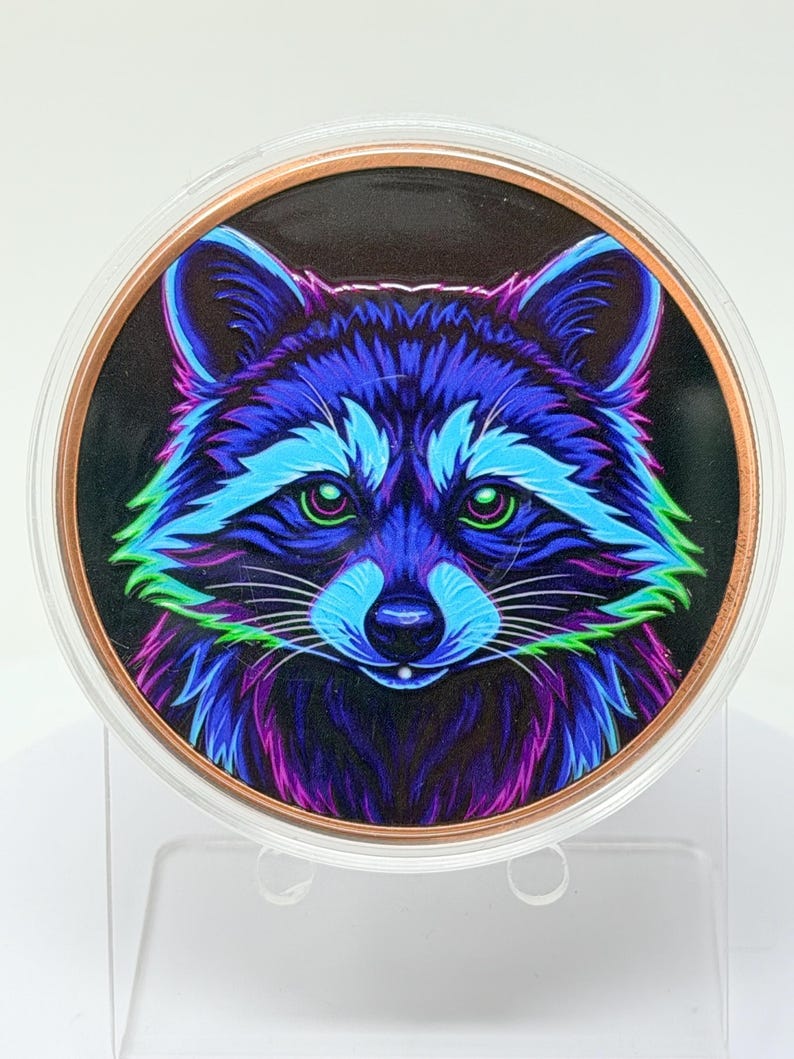 May include: A circular medallion featuring a vibrant, neon-colored illustration of a raccoon face. The raccoon is rendered in shades of electric blue, bright purple, and lime green against a black background, encased in a clear, round frame.