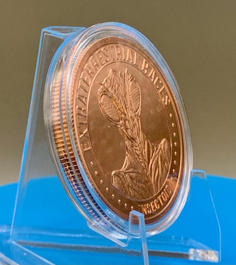 Tilted side view of the Intaglio Mint Insectoid 1 oz copper round in its clear capsule on a stand, showing the thickness and raised rim of the round and the EXTRATERRESTRIAL RACES obverse design.