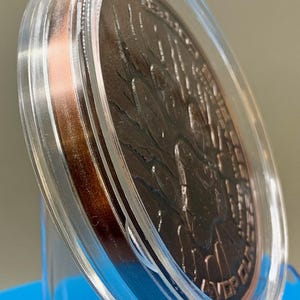 Angled edge view of the paw print reverse in the acrylic capsule, showing the thickness of the 5 oz copper round
