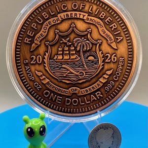 Reverse side of the Día de los Muertos legal tender copper coin marked "Republic of Liberia" and "One Dollar," shown next to the shop's alien figurine and a silver dime for scale