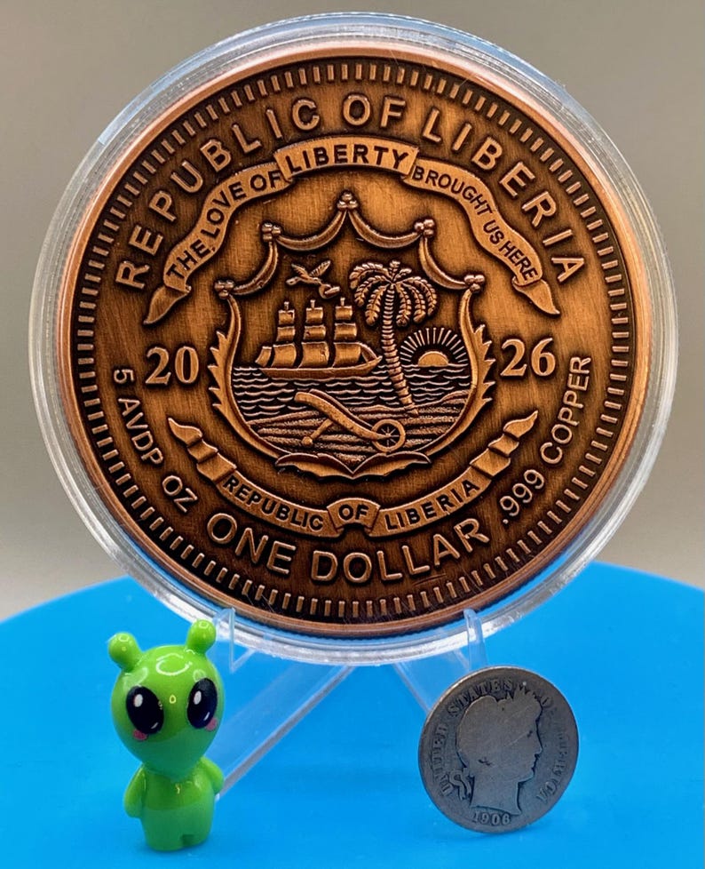 Reverse side of the Día de los Muertos legal tender copper coin marked "Republic of Liberia" and "One Dollar," shown next to the shop's alien figurine and a silver dime for scale