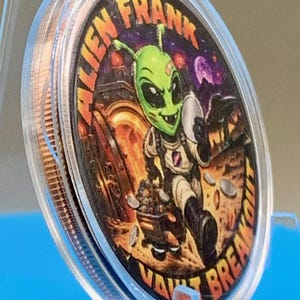 Angled side view of the Alien Frank Vault Breakout 1 oz copper round in its clear capsule on a blue stand, showing the colorized green alien artwork and the thick edge of the round.
