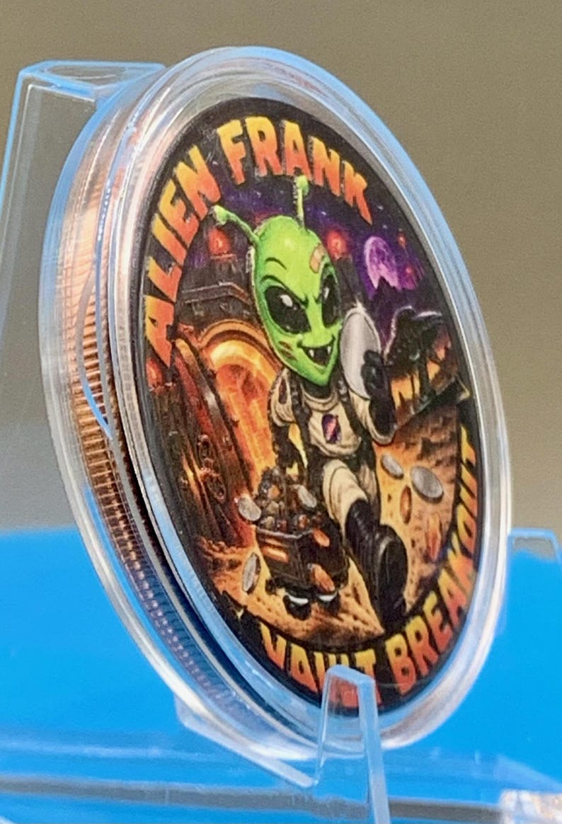 Angled side view of the Alien Frank Vault Breakout 1 oz copper round in its clear capsule on a blue stand, showing the colorized green alien artwork and the thick edge of the round.