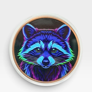 May include: A circular decorative item featuring a vibrant, neon-colored illustration of a raccoon face. The raccoon is rendered in shades of electric blue, purple, and bright green against a dark background, enclosed in a clear, circular frame.