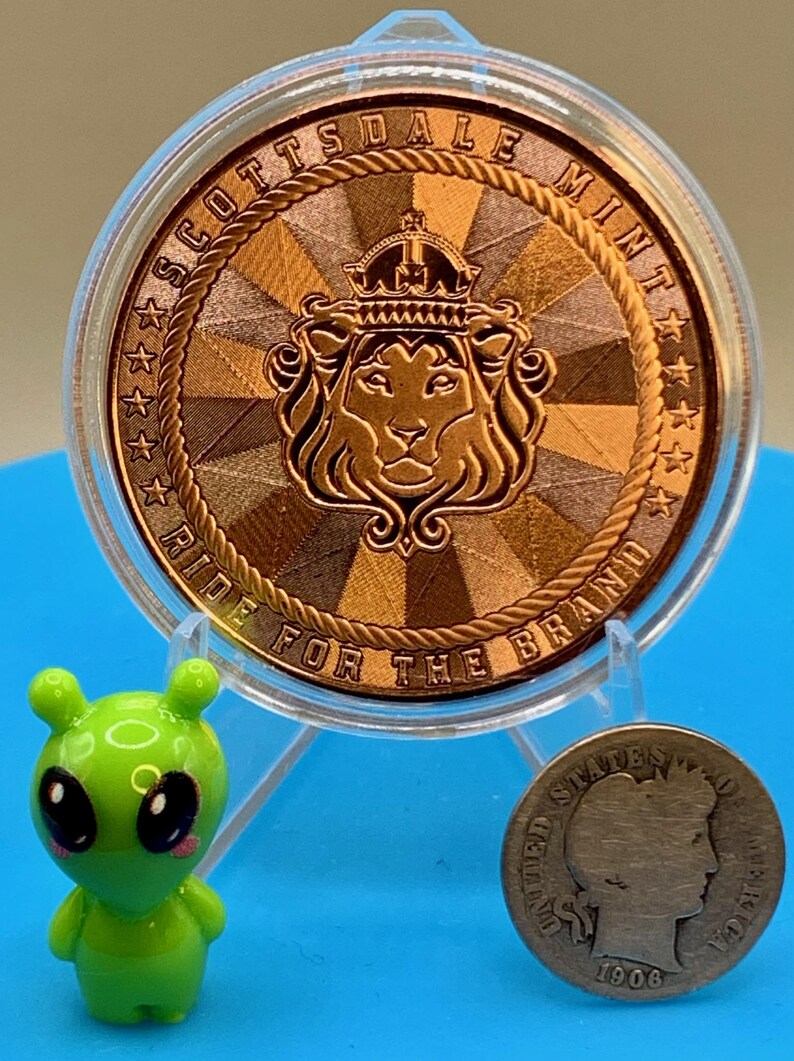 5 oz copper round with Scottsdale Mint lion crest reverse design and the motto "Ride for the Brand," shown with a small toy figure and a coin for size reference.