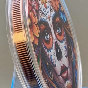 Angled edge view of the Día de los Muertos legal tender copper coin in a clear capsule, showing the coin's thickness and edge detail