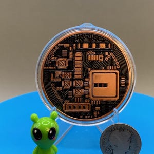 A circular copper-colored Bitcoin round featuring a black circuit board pattern, encased in a clear plastic protective holder. Beside it stands a small, bright green alien figurine and a silver-colored 1908 United States Barber dime.