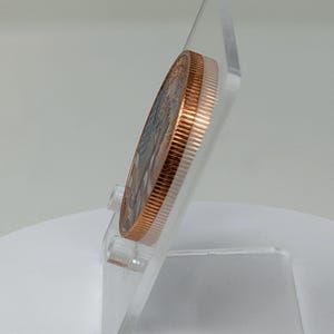 Edge-on side profile of the 1 oz copper round on a clear acrylic stand, showing the coin's thickness and smooth rim