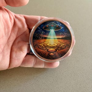 Close-up hero image of a 5 oz colorized copper bullion round featuring alien spacecraft, glowing beam, and crop circle design.