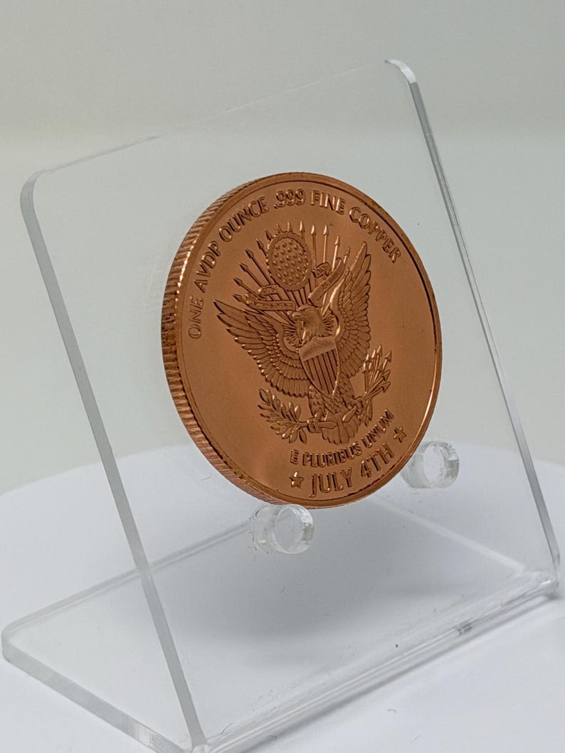 Angled rear view of the 1 oz copper round showing the Great Seal eagle reverse, tilted on a clear acrylic stand