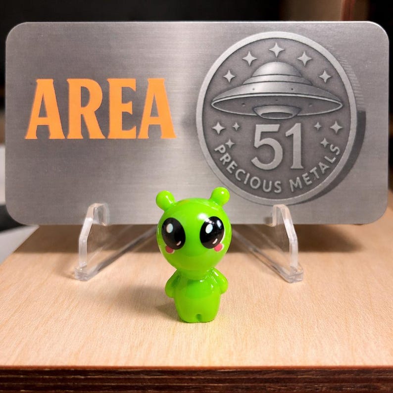 Area 51 Precious Metals branding card with green alien mascot figurine, featuring the shop's UFO logo