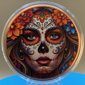 Close-up of the Día de los Muertos legal tender copper coin with a colorful sugar skull face design in a protective capsule