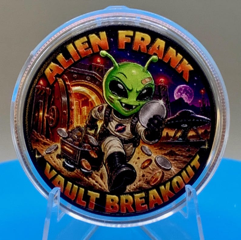 Front of the Alien Frank Vault Breakout 1 oz copper round in a clear capsule, showing a colorized green alien in a space suit pushing a cart of coins through a vault, in orange, red and purple, with "Alien Frank" across the top and "Vault Breakout" along the bottom edge.