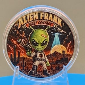 Front of the First Contact 1 oz copper round in a clear capsule: a colorized green grey alien in a spacesuit holding a raygun beneath a UFO over a red desert sunset, with "Alien Frank First Contact" lettering