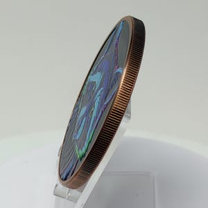 May include: A circular copper-toned coin with a reeded edge, featuring a stylized graphic of a wolf face in shades of blue, purple, and green against a black background. The coin is displayed at an angle, showing its thickness and metallic rim.