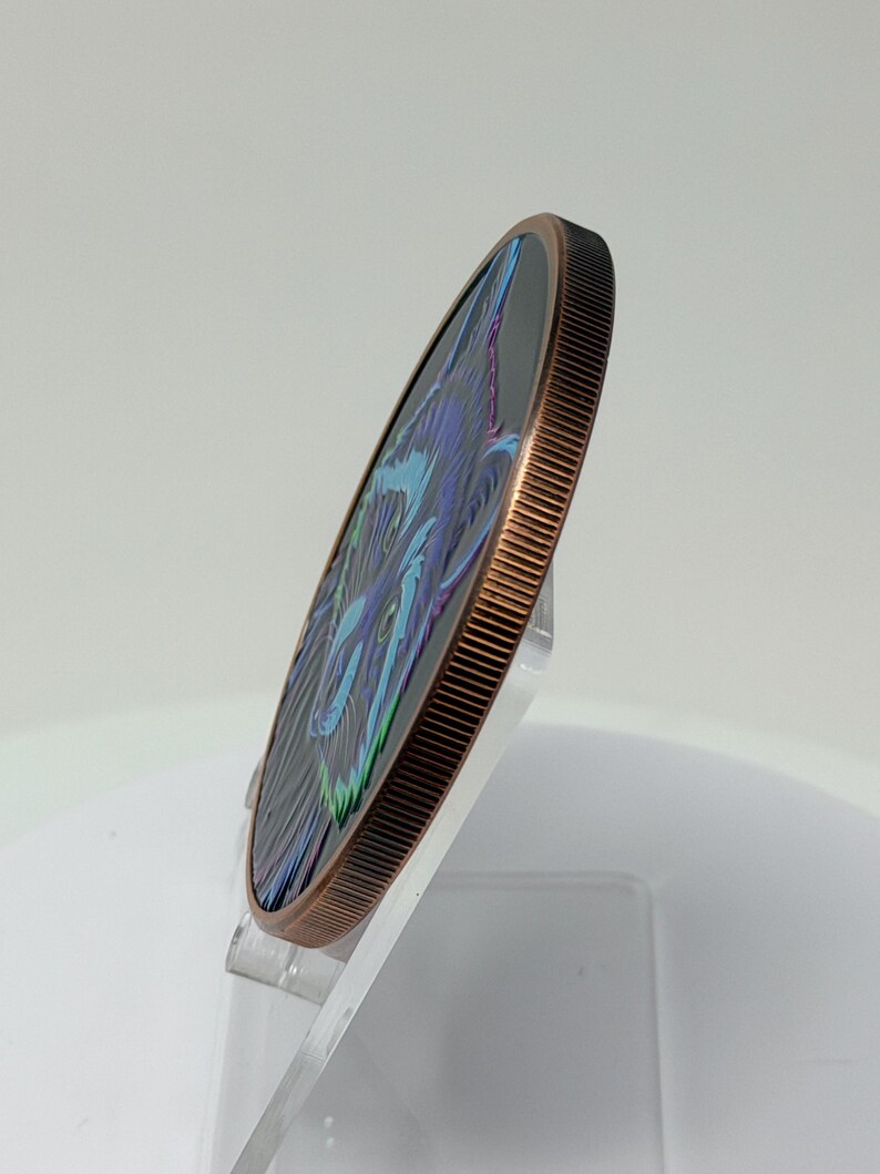May include: A circular copper-toned coin with a reeded edge, featuring a stylized graphic of a wolf face in shades of blue, purple, and green against a black background. The coin is displayed at an angle, showing its thickness and metallic rim.