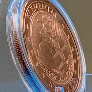 Angled side view of the Night Arrival 1 oz copper round in its capsule, showing the copper reverse and the thickness of the coin