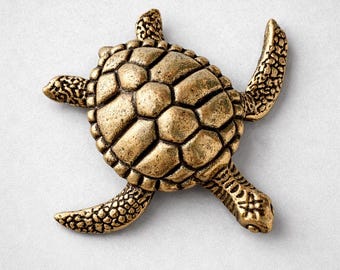 Peut inclure: Figurine de tortue dorée avec une carapace texturée et des nageoires détaillées. La carapace de la tortue présente un motif de formes hexagonales. La figurine est en métal et se détache sur un fond blanc.