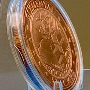 Side view of the First Contact 1 oz copper round in its capsule showing the bright copper reverse and the coin thickness