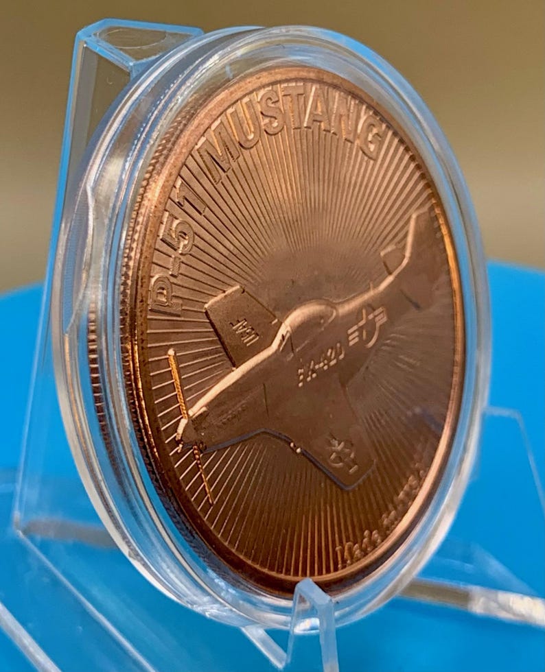 Tilted front view of a 1 oz .999 fine copper round in a display capsule, showing the P-51 Mustang design and round edge at an angle, on a blue background.
