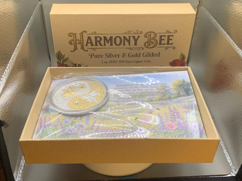 Open Harmony Bee copper round packaging box showing the round nested in its capsule on top of a printed certificate insert, with the box lid visible in the background.