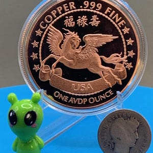 Encapsulated 2026 Year of the Horse copper round on a blue stand, Pegasus reverse showing, flanked by the Area 51 Precious Metals green alien mascot figurine and a silver Barber dime for scale.