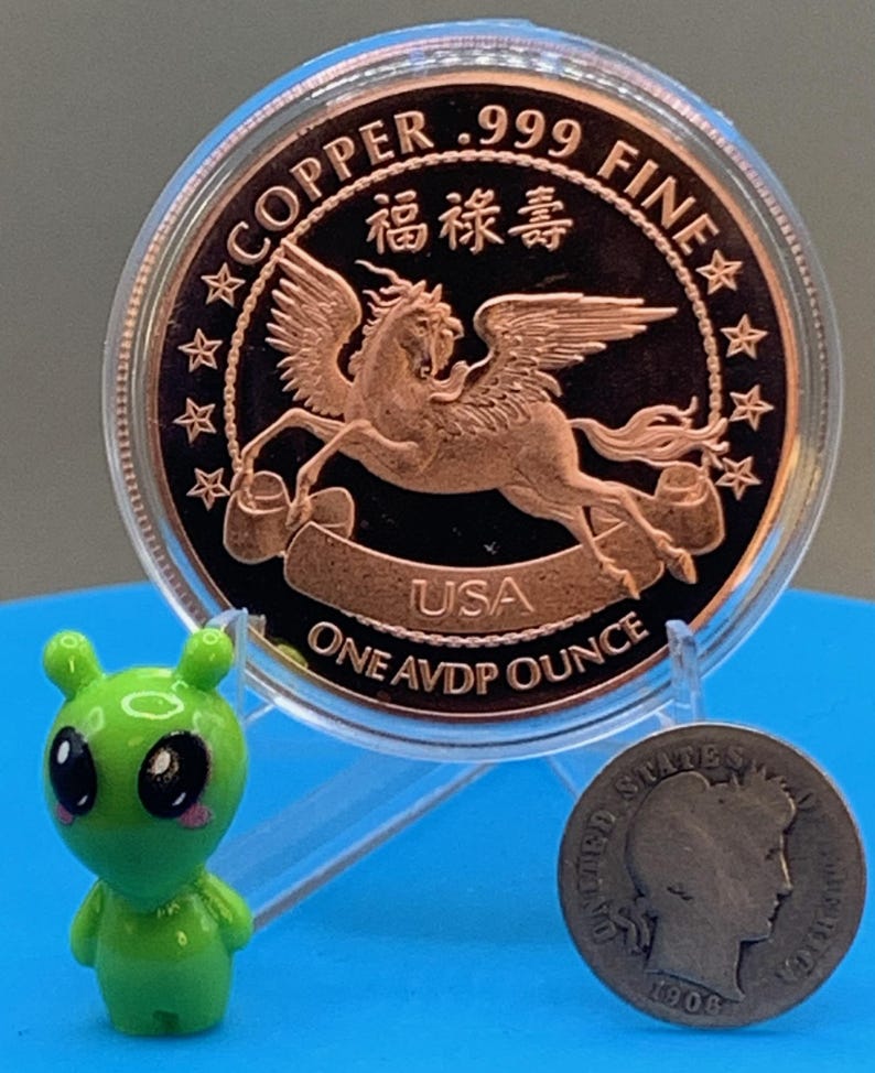 Encapsulated 2026 Year of the Horse copper round on a blue stand, Pegasus reverse showing, flanked by the Area 51 Precious Metals green alien mascot figurine and a silver Barber dime for scale.