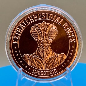 Obverse of the Intaglio Mint Insectoid 1 oz .999 copper round showing a mantis-style alien head with large compound eyes, framed by the legend EXTRATERRESTRIAL RACES and the word INSECTOID, displayed in a clear capsule on a blue stand.