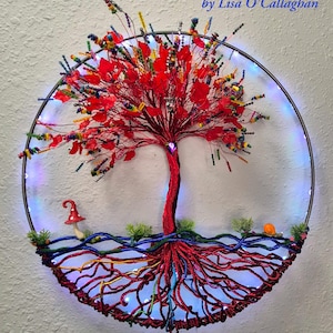 May include: A handcrafted, circular wall art piece featuring a vibrant red tree with a textured trunk and leaves. The tree's roots are intricately designed, and the piece is illuminated with LED lights. The artwork includes the text "Handmade With Love by Lisa O'Callaghan."