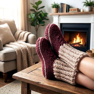 Può includere: Pantofole lavorate a maglia bordeaux e beige con un motivo strutturato. Le pantofole sono su un tavolo di legno, con un camino sullo sfondo. Queste pantofole sono un accessorio caldo e confortevole per rilassarsi a casa.