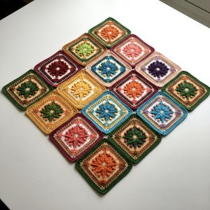 May include: A collection of sixteen colorful, crocheted squares arranged in a diamond pattern. Each square features a central floral design in various colors, including orange, pink, green, and blue, surrounded by contrasting borders. The squares are displayed on a white surface.