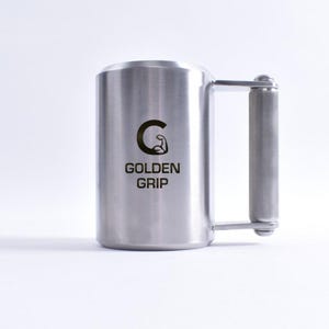Może przedstawiać: Kubek ze stali nierdzewnej z uchwytem. Na kubku widnieje czarny napis "GOLDEN GRIP" oraz grafika sztangisty. Kubek jest cylindryczny i ma teksturowany uchwyt. Wysokość około 15 cm.
