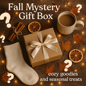 May include: A fall-themed gift box with a beige ribbon, surrounded by fall leaves, a mug of coffee, a pair of socks, and cinnamon sticks. The text reads "Fall Mystery Gift Box" and "cozy goodies and seasonal treats."