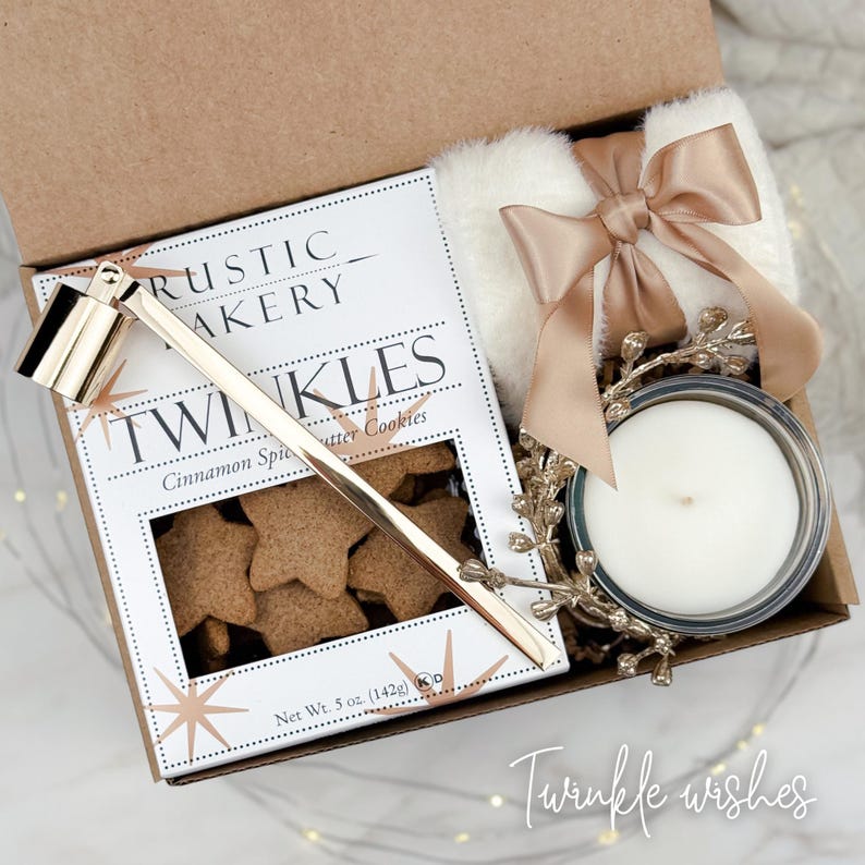 May include: A gift box containing a box of star-shaped cinnamon spice butter cookies, a white fluffy item tied with a gold ribbon, a candle, and a gold-colored candle snuffer. The box is labeled "Rustic Bakery Twinkles". The text "Twinkle wishes" is written on the bottom right.