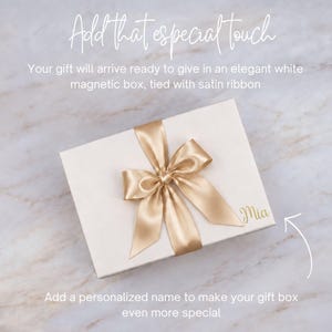 May include: A rectangular white magnetic gift box featuring a gold satin ribbon tied in a bow on top. The name Mia is printed in gold script on the lower right corner of the lid. Text on the image reads Add that especial touch, Your gift will arrive ready to give in an elegant white magnetic box, tied with satin ribbon, and Add a personalized name to make your gift box even more special.