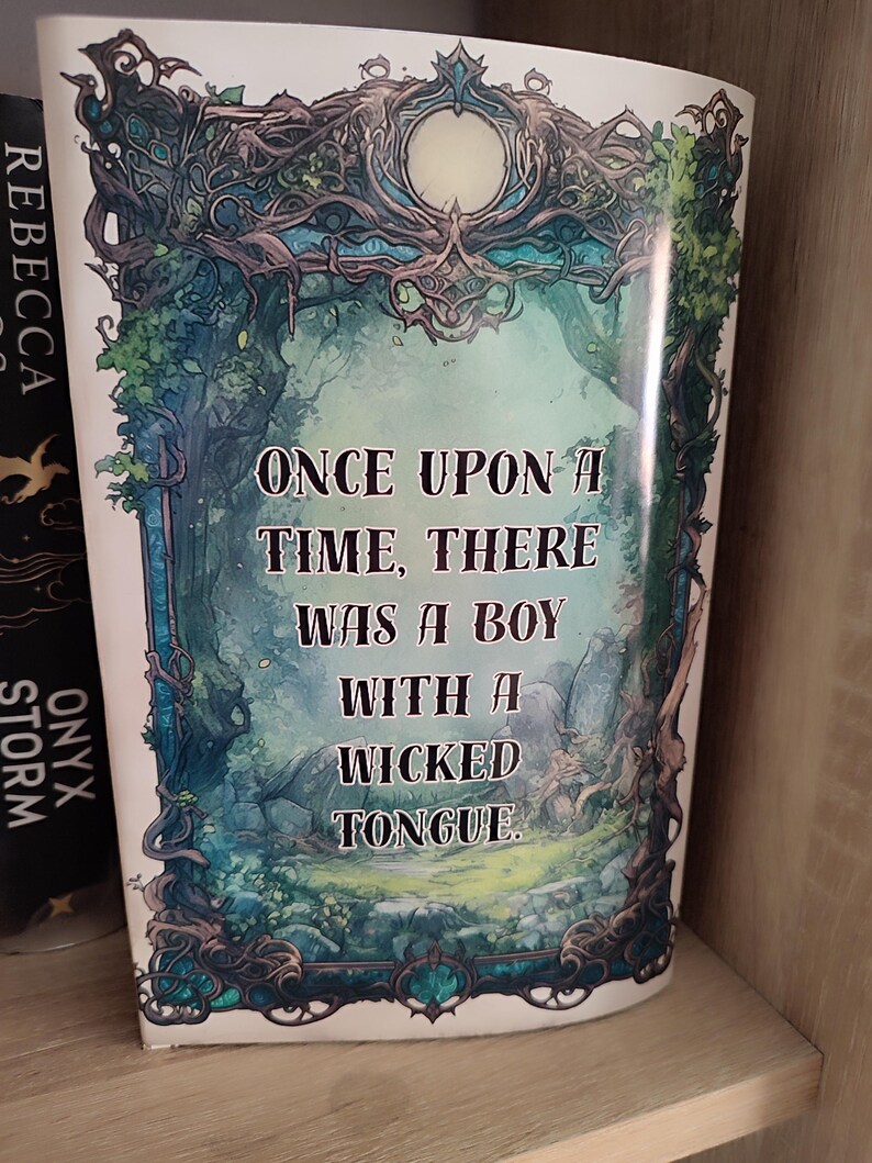 May include: A book cover with the text "ONCE UPON A TIME, THERE WAS A BOY WITH A WICKED TONGUE." The cover features a fantasy illustration with a forest scene in shades of green and blue, framed by ornate, vine-like details. The book is on a shelf.
