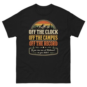 May include: A black short-sleeved t-shirt featuring a graphic with a mountain landscape and the text: OFF THE CLOCK, OFF THE CAMPUS, OFF THE RECORD, and If you saw me at Walmart, no you didn't. The design uses orange, yellow, and white colors.