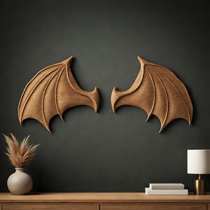 May include: Two wooden dragon wing wall art pieces. Each wing is carved with detailed veining and a curved shape. The wings are a warm brown color and mounted on a dark gray wall. The wings are a decorative element.